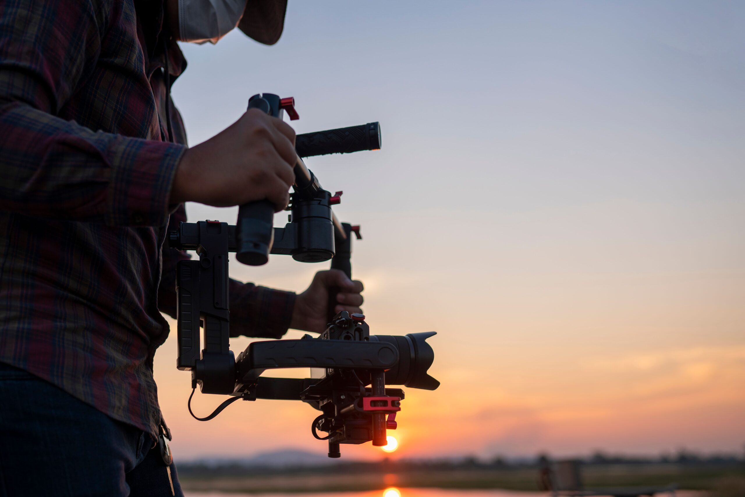 A closeup of a filmmaker using a gimbal stabilizer and a camera at sunset