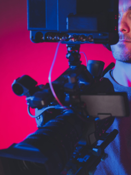 Video Production Stage Dark Red and Blue Illuminated and Film Making Professional Digital Camera Operator at Work. Caucasian Men in His 40s.